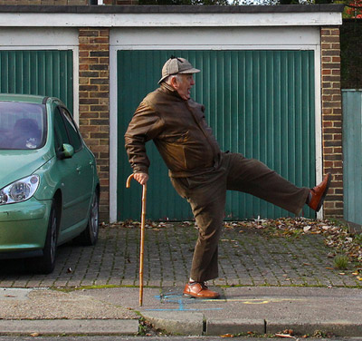 A funny old man dancing in the street with his wooden cane